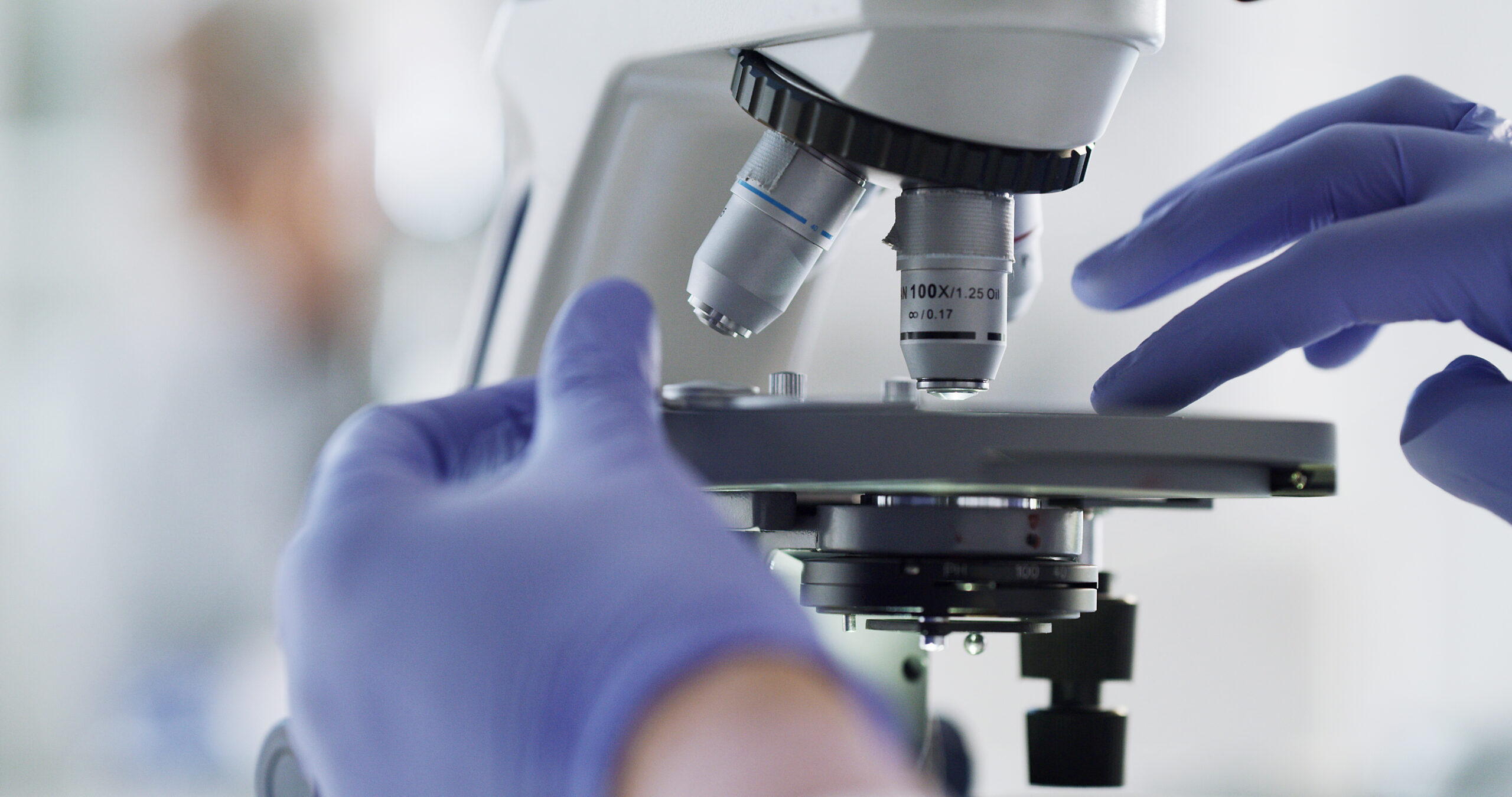 Close up of a scientist's gloved hands adjusting a sample on a microscope